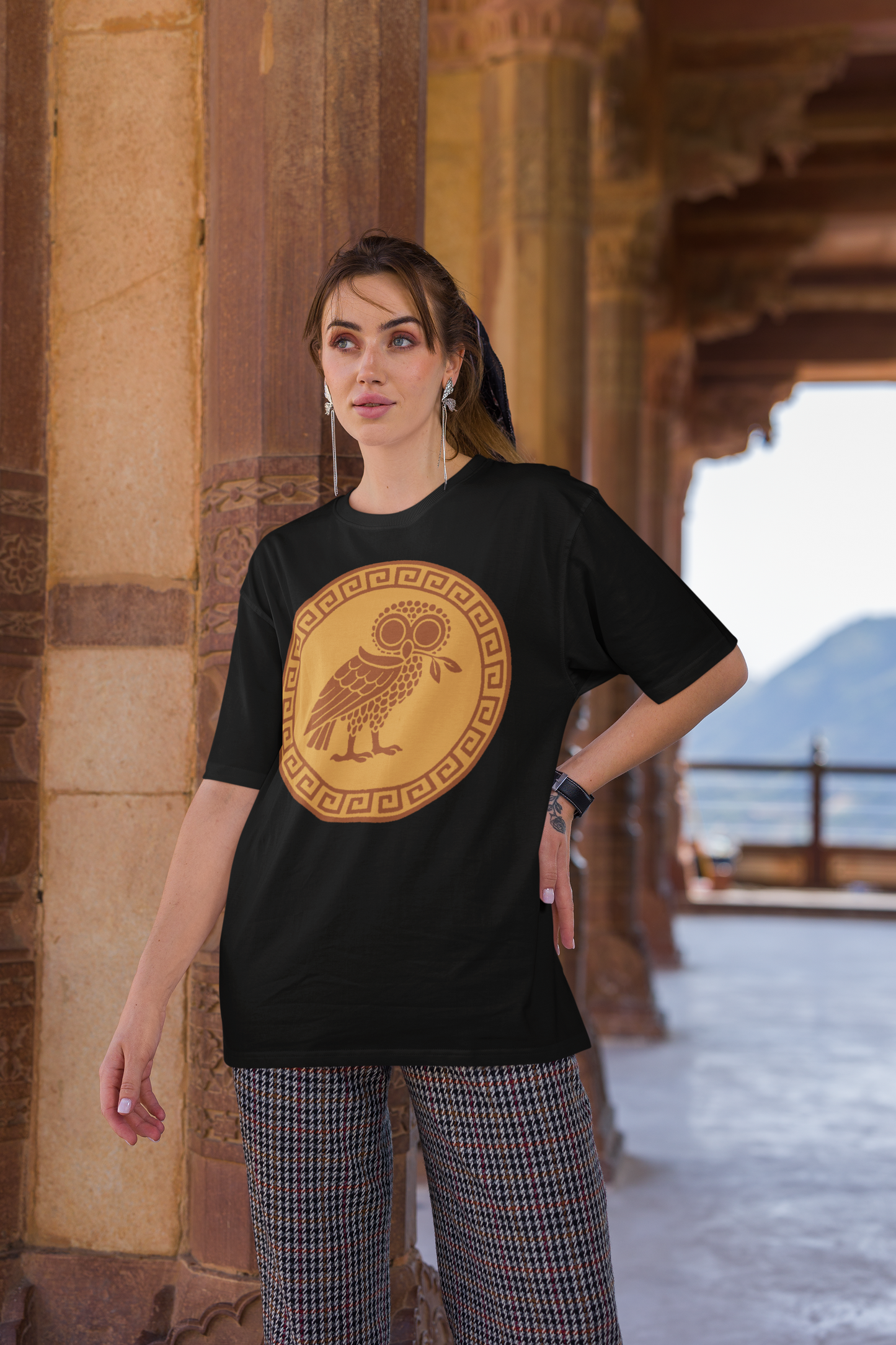 Woman wearing a black graphic t-shirt with a yellow owl and greek key design in an ancient temple setting