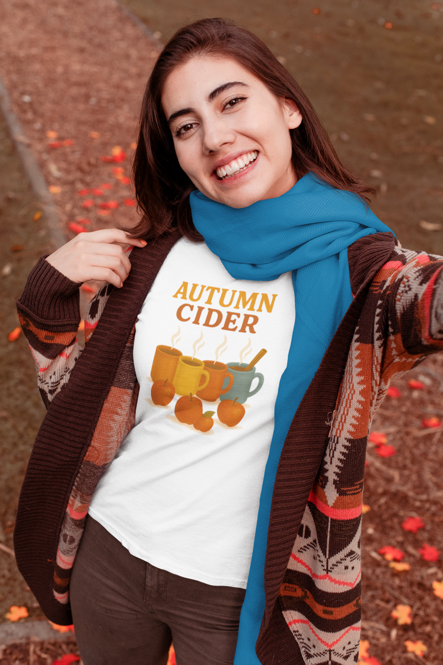 Autumn Cider T-Shirt – Cozy Fall Graphic Tee with Steaming Mugs worn by a smiling woman in a fall outfit and sage green scarf, surrounded by autumn leaves