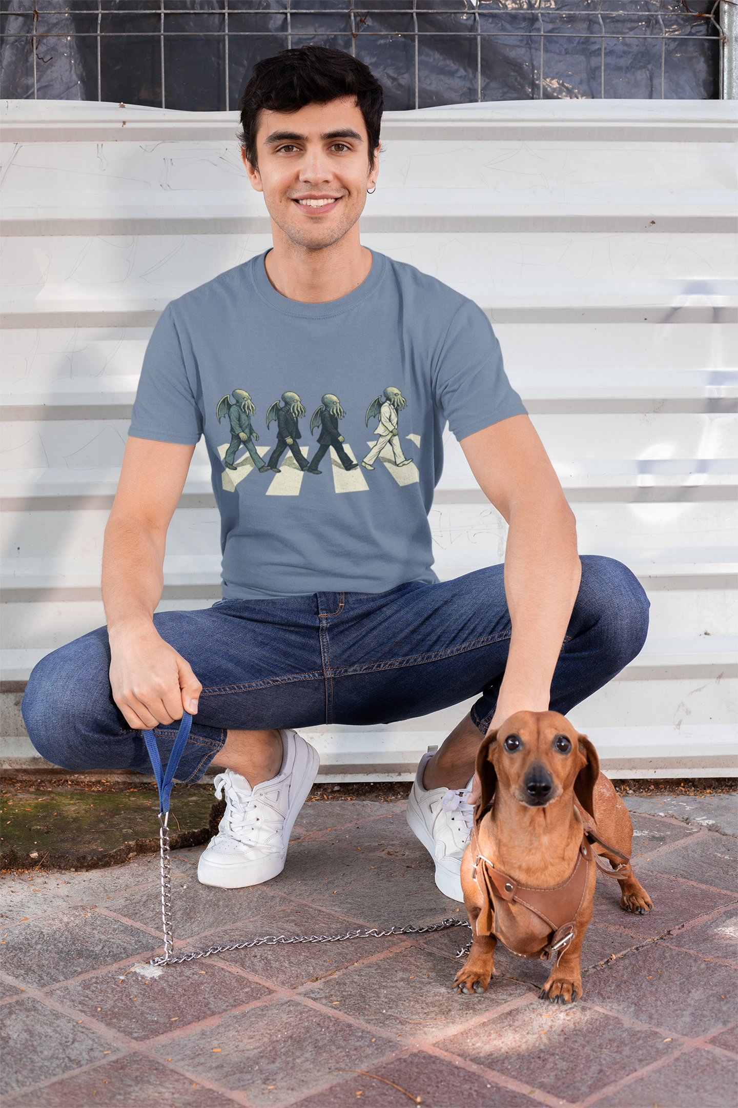 Man sitting on steps with a dachshund wearing a Cthulhu Crossing T-shirt in heather indigo from whimspin.