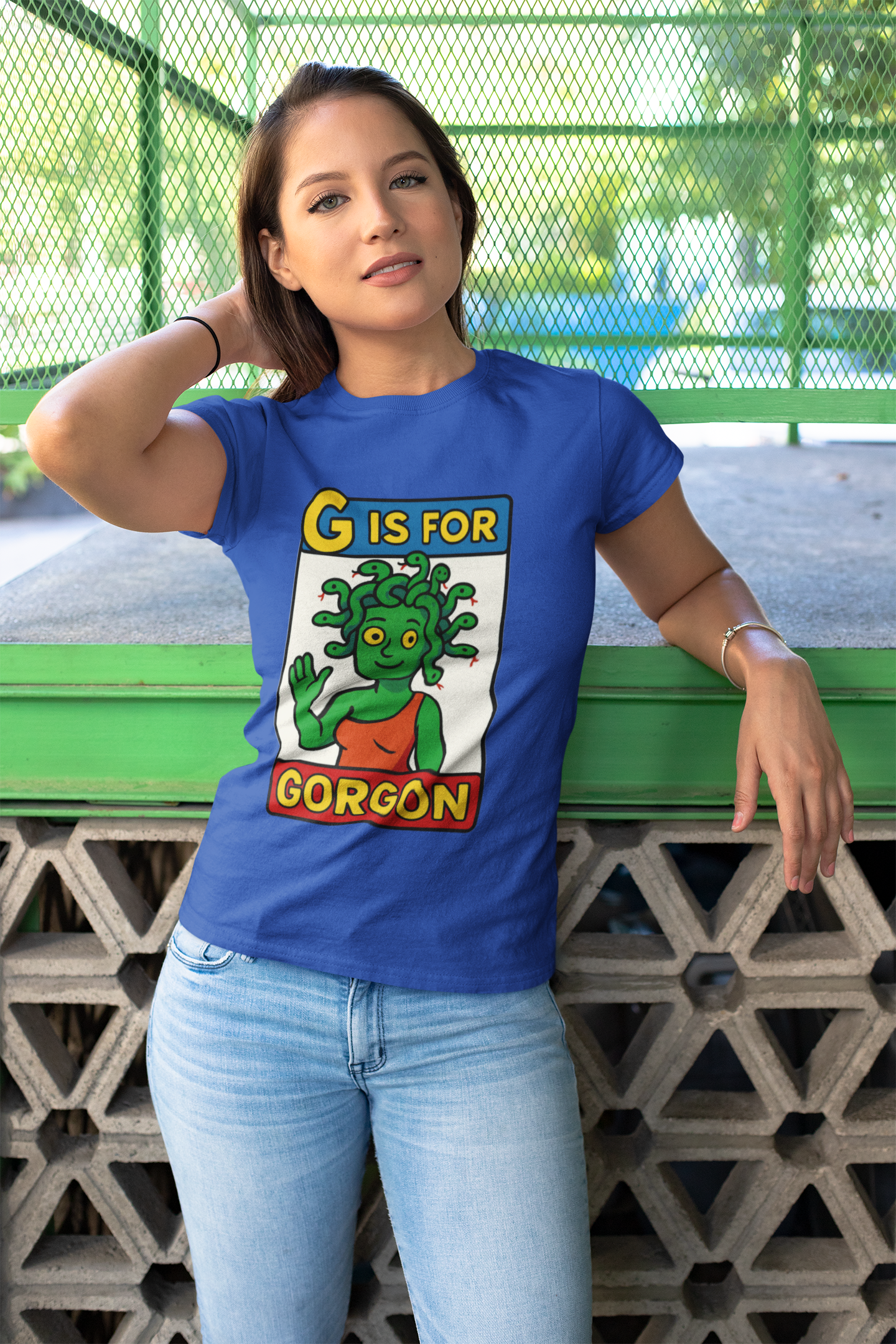 Woman outdoors wearing the G is for Gorgon T-Shirt in blue, a halloween gorgon shirt with playful cartoon gorgon head artwork.