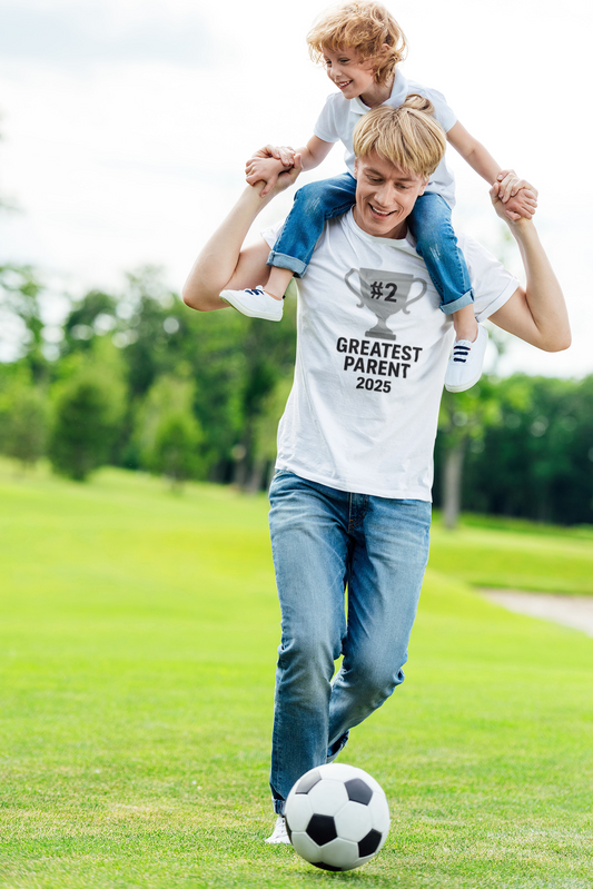 #2 Greatest Parent 2025 T-Shirt in white, worn by smiling dad giving shoulder ride to young child while kicking soccer ball, a humorous second place parent shirt for active parents with a sense of humor.