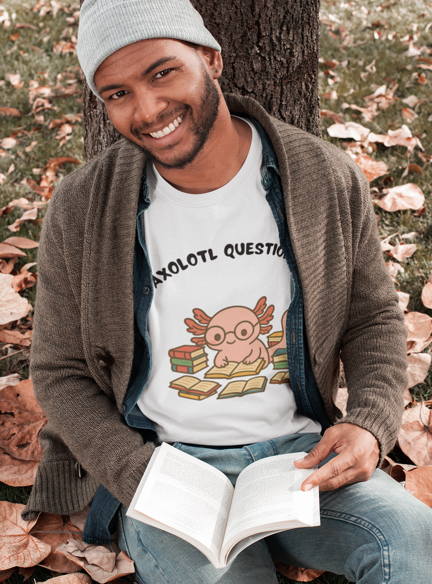 Man sitting on the ground with an open book, wearing a t-shirt with a cartoon axolotl design.