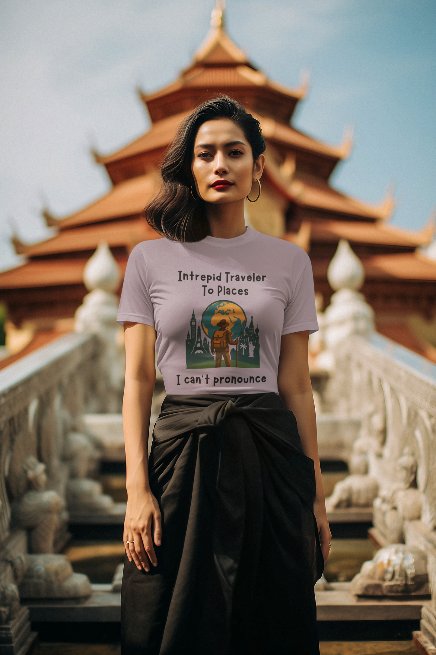 Woman wearing a t-shirt with graphic design of a traveler standing in front of the silhouettes of world landmarks and a globe with the text "Intrepid Traveler to Places I Can't Pronounce" in front of a traditional Asian building.