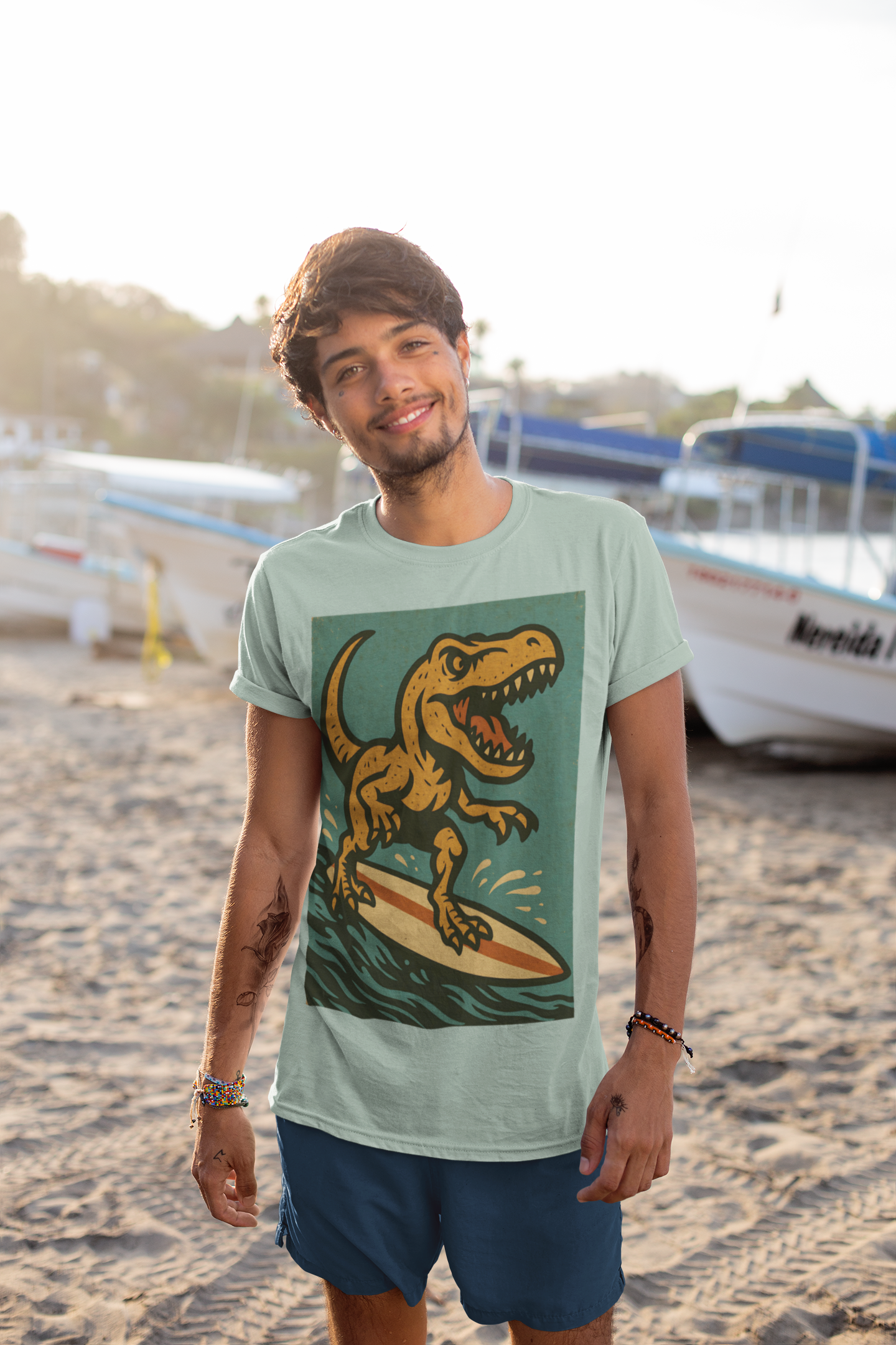 A man wearing the Surfing T-Rex T-Shirt – Funny Dinosaur Graphic Tee for Summer Vibes from WhimSpin stands on a beach with boats in the background. The image on the shirt features an orange T-rex roaring while riding a yellow surfboard on top of waves.