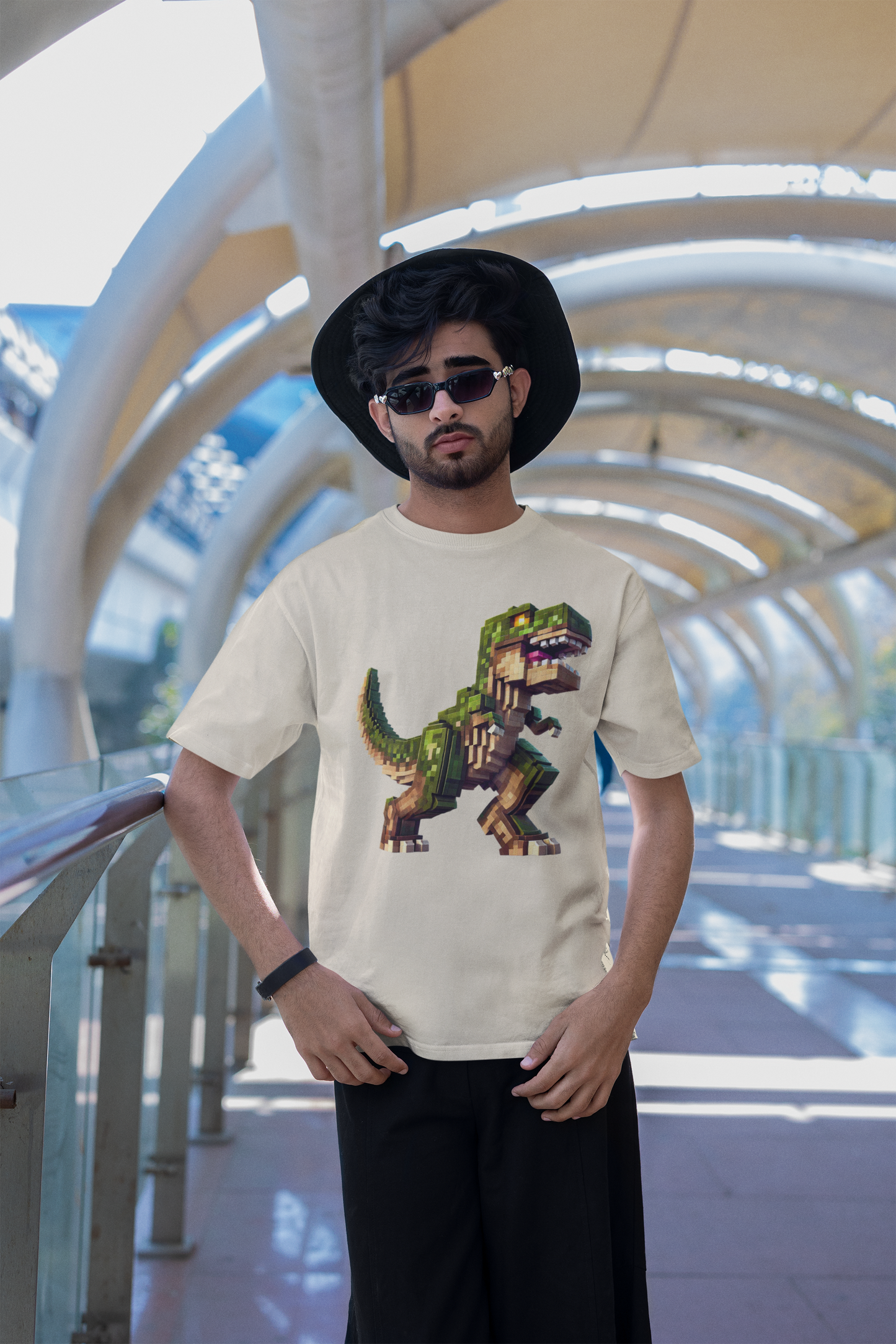Pixel Dinosaur Graphic T-Shirt – Retro Unisex Tee for Adult Dino Fans in cream, worn by man with bucket hat and sunglasses in architectural bridge space.