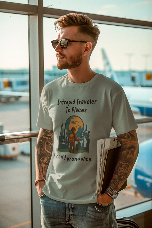 Man wearing a t-shirt with a graphic design of a traveler standing in front of the silohuettes of world landmarks and a globe with the text "Intrepid Traveler to Places I Can't Pronounce", standing in an airport.
