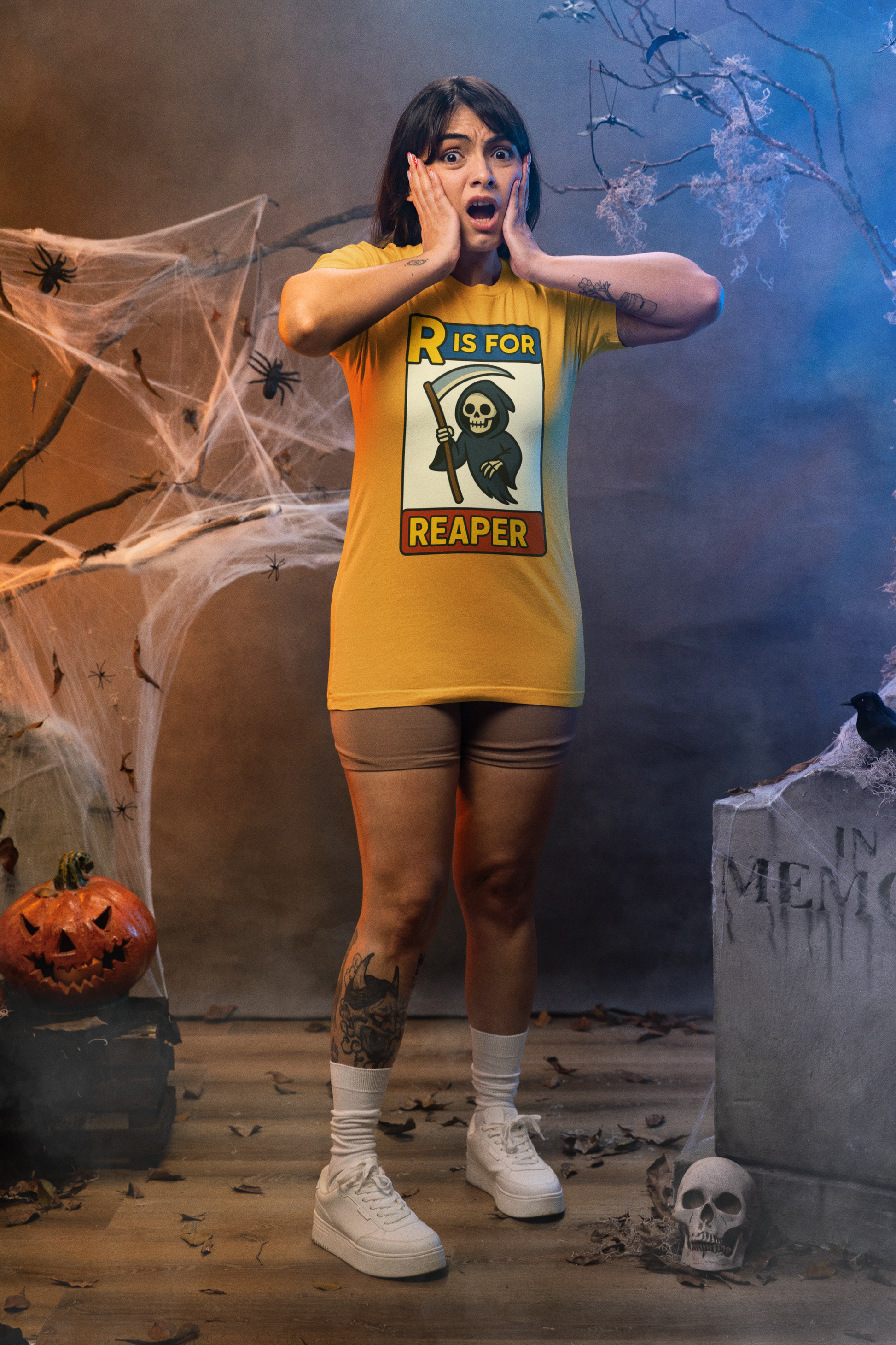 R Is For Reaper T-Shirt – Cute Grim Reaper Shirt from the Monster Alphabet Series, worn by a shocked woman in a spooky Halloween set with cobwebs and tombstones