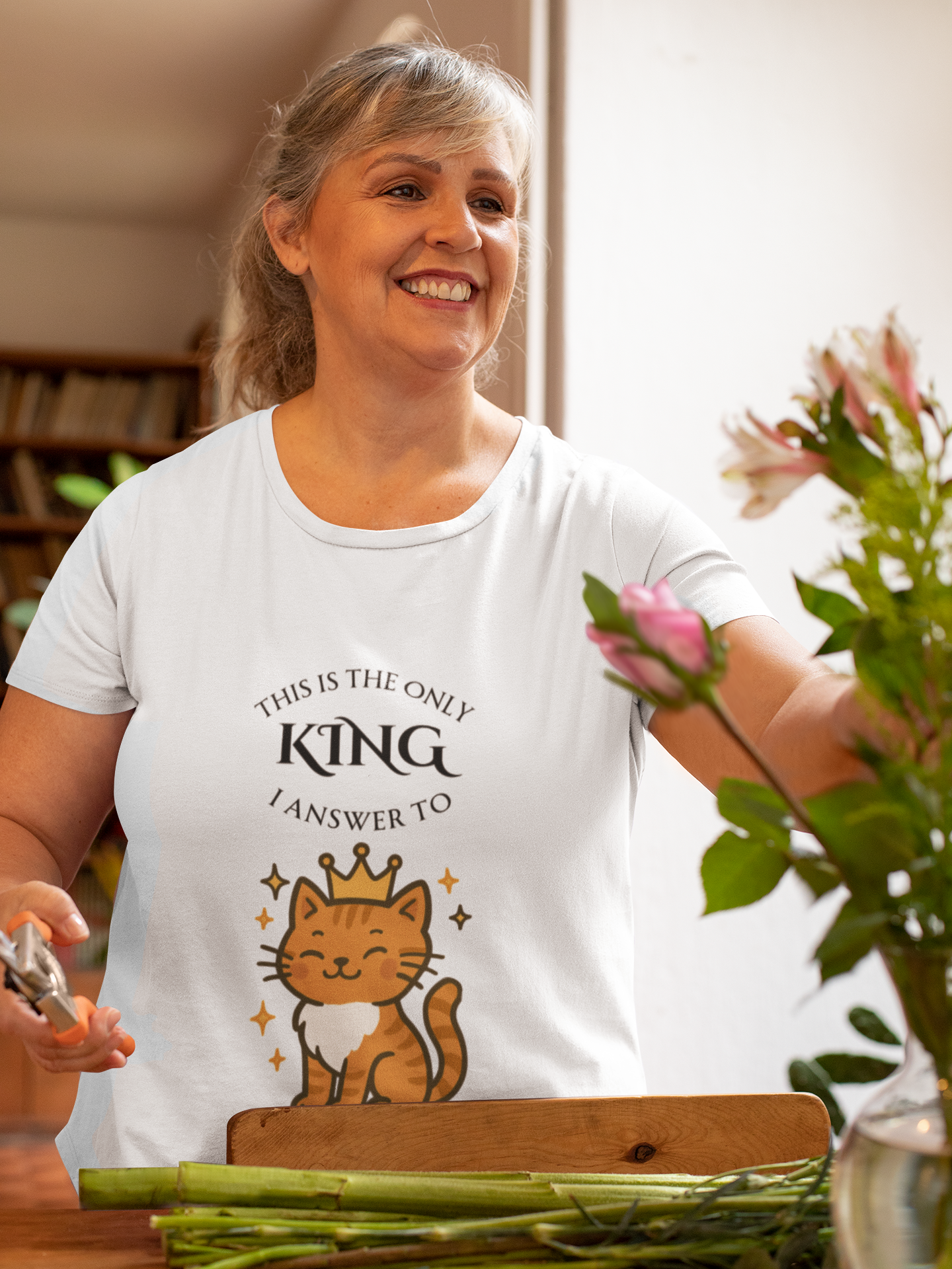 Middle aged woman putting flowers in a vase wearing "The Only King I Answer To" T-Shirt from WhimSpin– Cute Cat Lady Tee