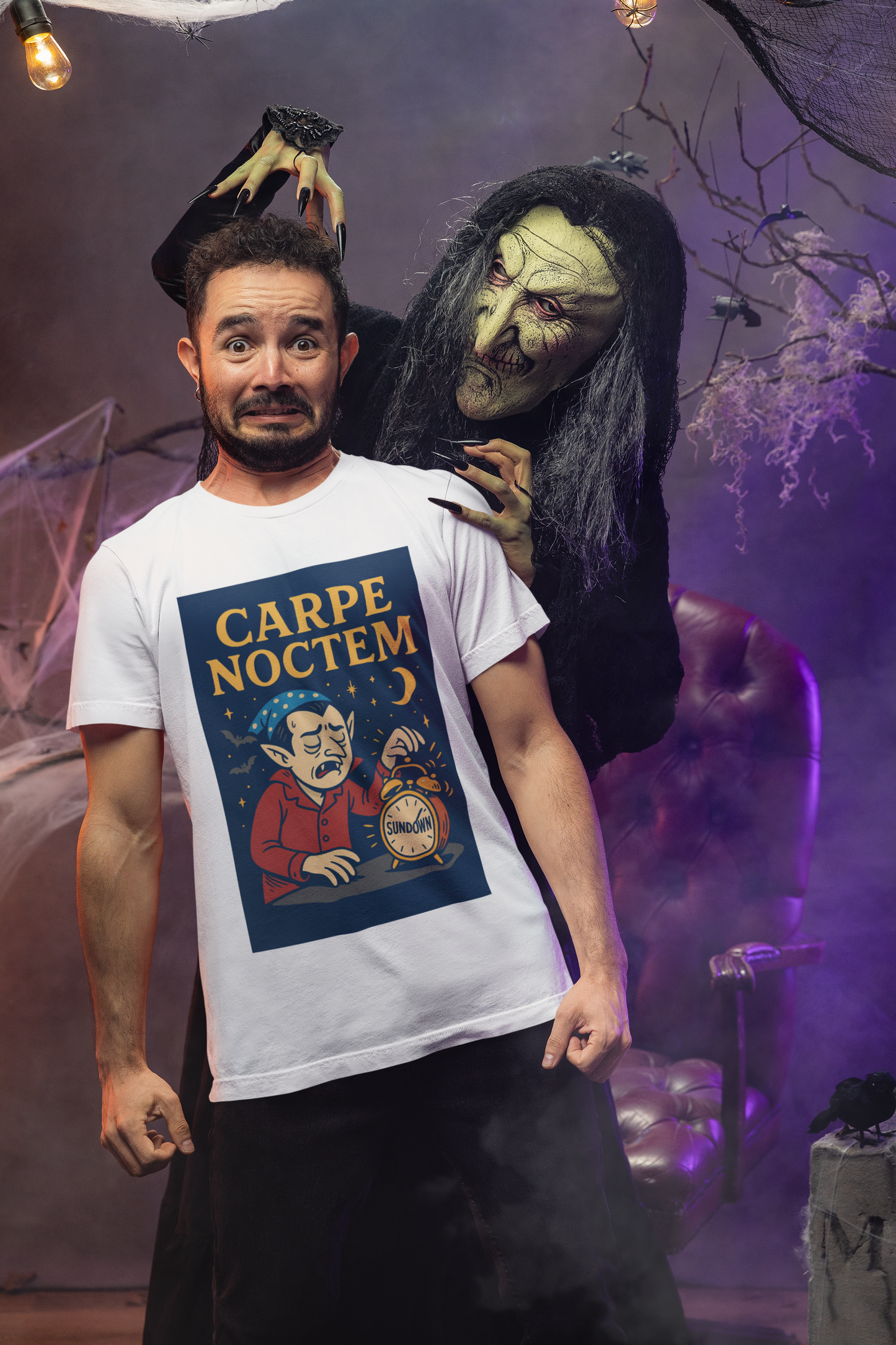 Person wearing a white t-shirt with a graphic design of a vampire struggling to wake up next to his alarm clock and a crescent moon and  the text "Carpe Noctem", stands in a haunted house about to be attacked by a green-faced halloween figure.