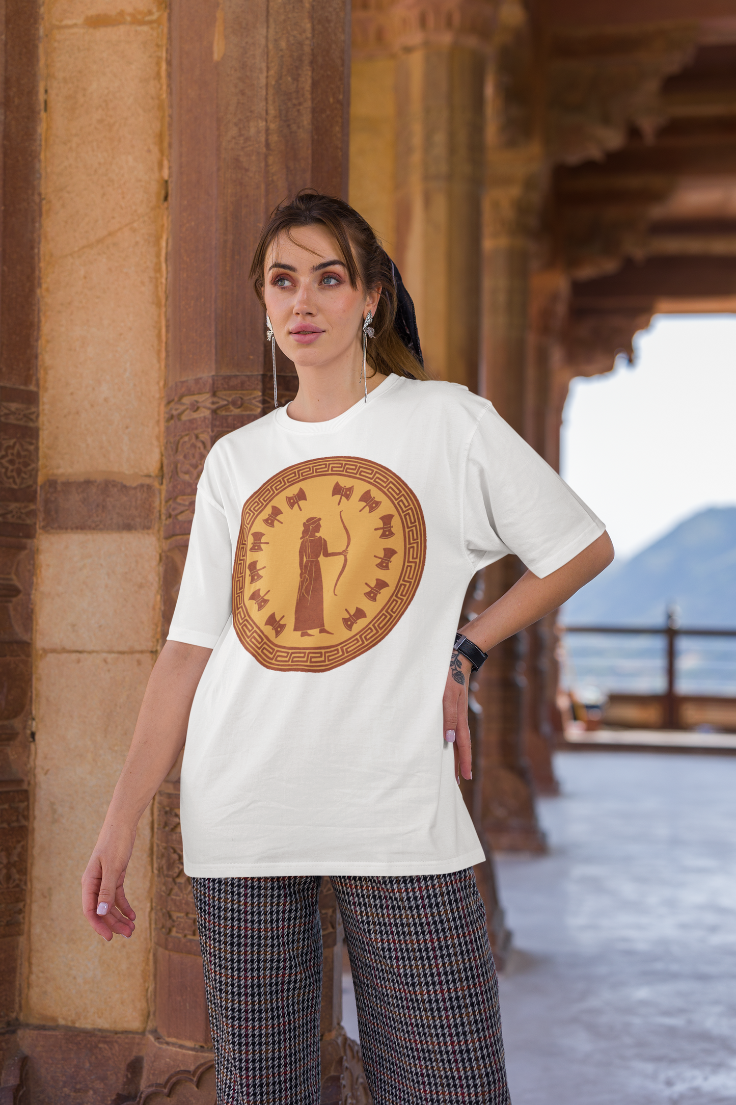 White Penelope Epic Queen of Ithaca T shirt from Whimspin. The shirt features an image of a woman in ancient Grecian robes holding a bow and surrounded by 12 axes. The images is in terracotta cotta red and gold in the style of ancient amphora art.