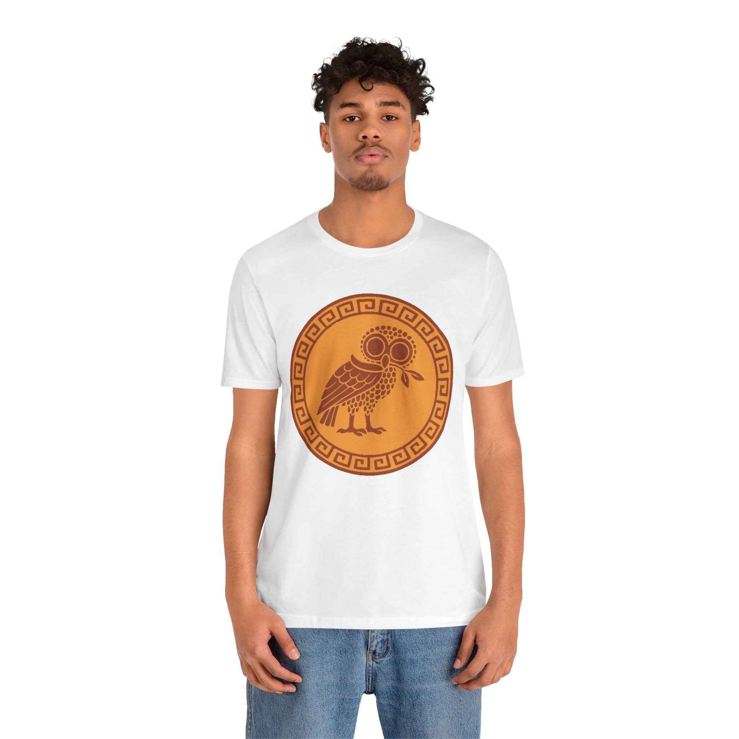 a man wearing a white tee shrt with a graphic image of a yellow/gold medallions encircled by the greek key design and an owl holding an olive branch in the center stands in front of a white back ground.