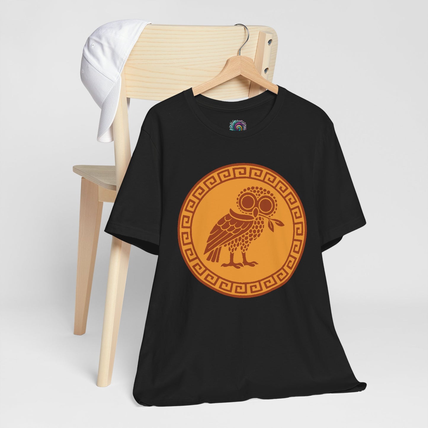 Black t-shirt with an orange owl design on a white background hangs on a hanger from the back of a chair
