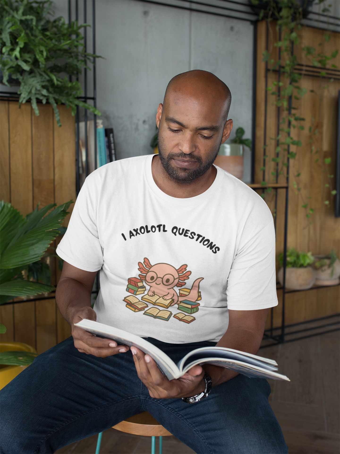 Man wearing a white t-shirt with a cartoon axolotl design and text, sitting and reading a book.