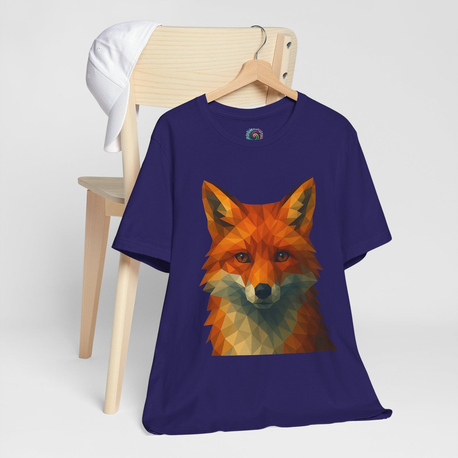 a geometric art red fox head on a navy blue shirt hangs on a hanger from the back of a wooden chair.