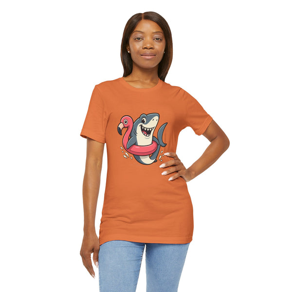 Orange crewneck T-shirt with shark and flamingo floatie graphic, model hands on hips.