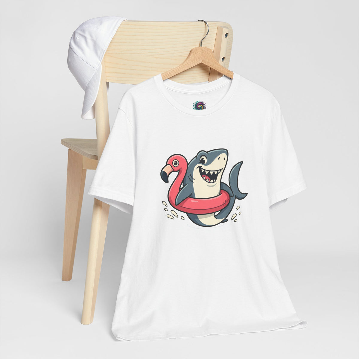 White crew-neck T-shirt with shark-and-flamingo float graphic, hanging on a wooden hanger