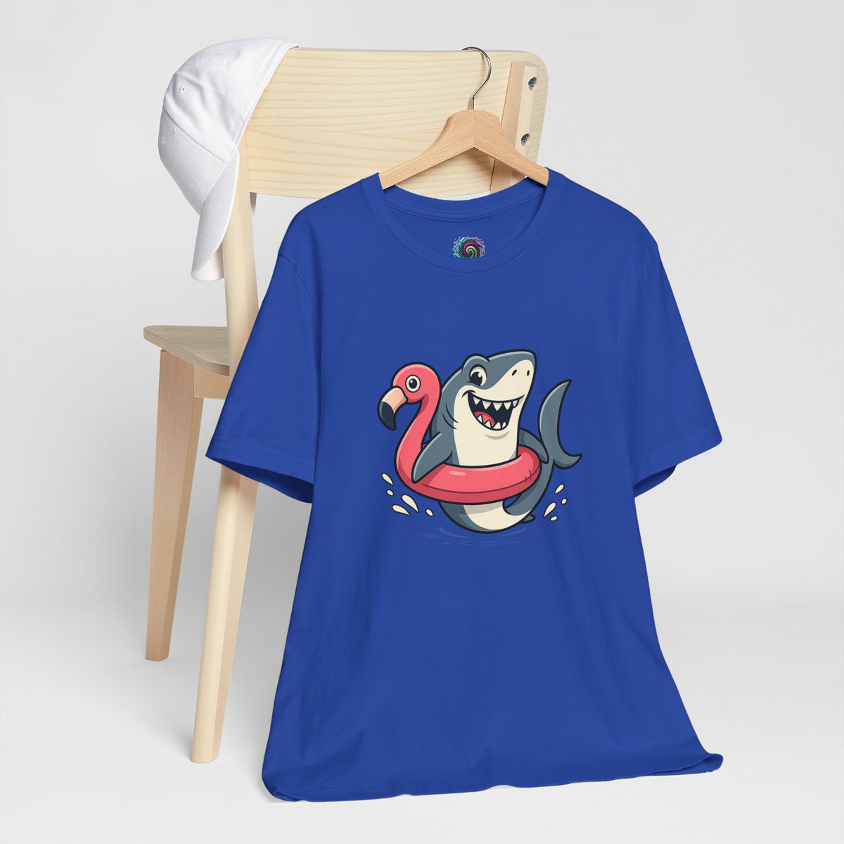 Royal blue t-shirt on a wooden hanger, featuring shark and flamingo float graphic