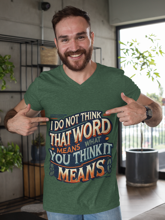 A caucasian man with brown hair and a beard wears a green Inigo Montoya t shirt with "I Don't Think That Word Means What You Think It Means" written on it. The man is smiling and points to thw words on his chest.