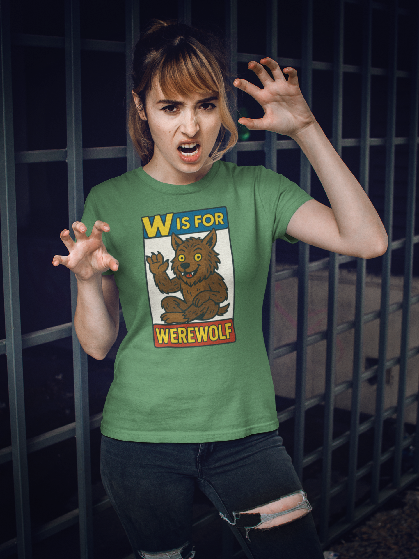 Person wearing a green t-shirt with a graphic design of a werewolf and text 'W is for Werewolf' in front of a metal fence.