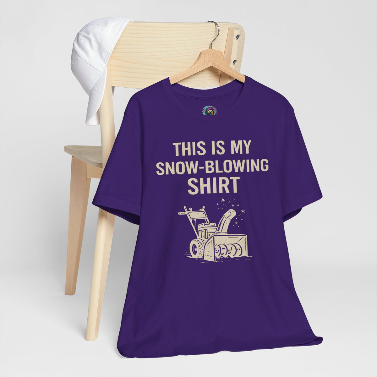 Purple graphic T-shirt on wooden hanger with snow blower illustration and winter chore slogan