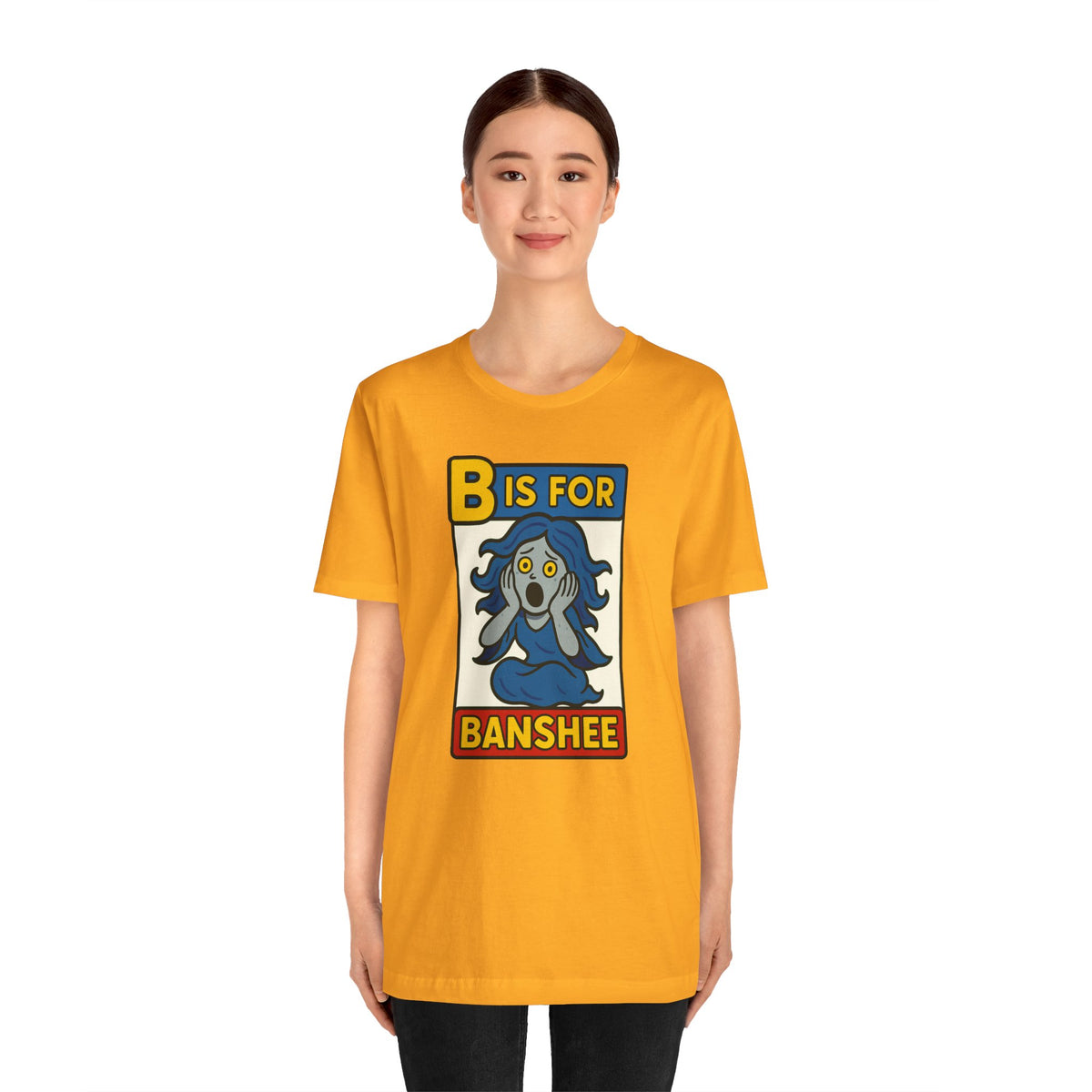 Gold crewneck T-shirt with “B is for Banshee” illustrated character square on front