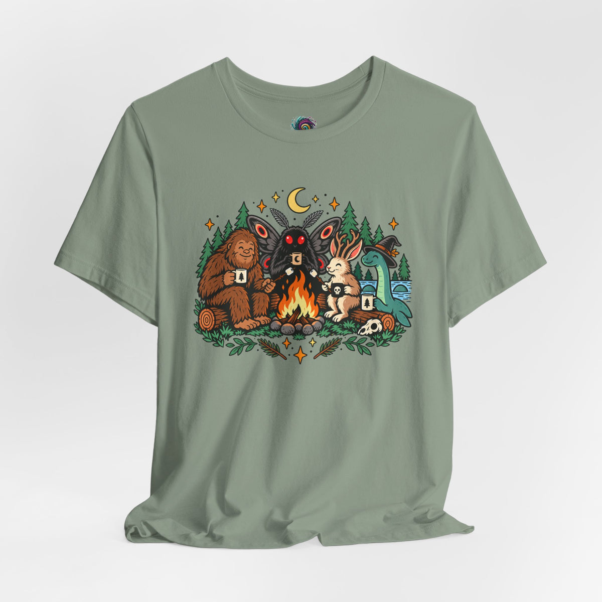 Sage green T-shirt with colorful campfire cryptid graphic centered on the chest