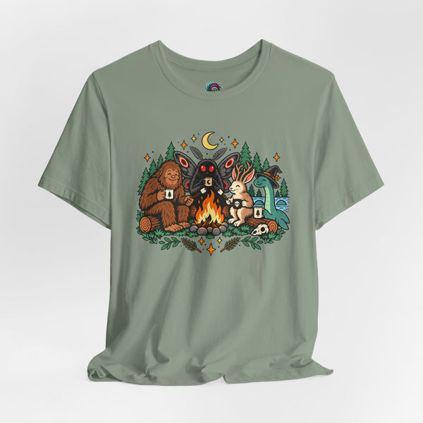 Sage green T-shirt with colorful campfire cryptid graphic centered on the chest