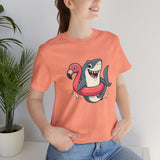 Coral crewneck T-shirt with shark and flamingo floatie illustration at center chest