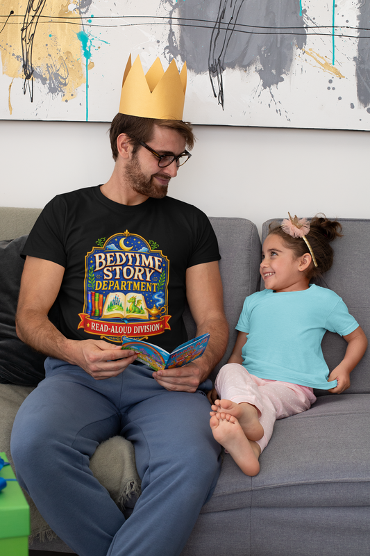 Man wearing a 'Bedtime Story Department - Read-Aloud Division' t-shirt and reading to a child on a couch.