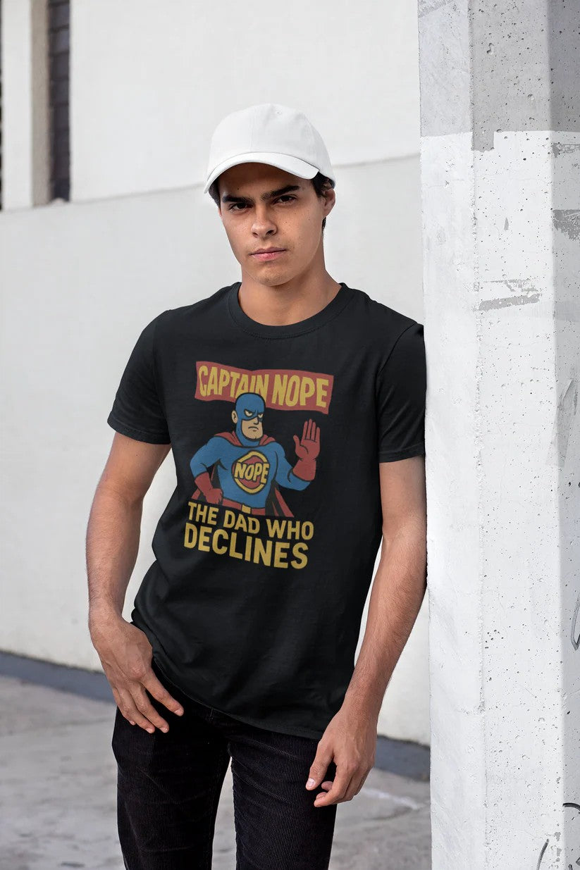 Young man in black Captain Nope Dad Shirt leaning casually against a white pillar, showcasing the comic-style superhero design and “The Dad Who Declines” slogan.