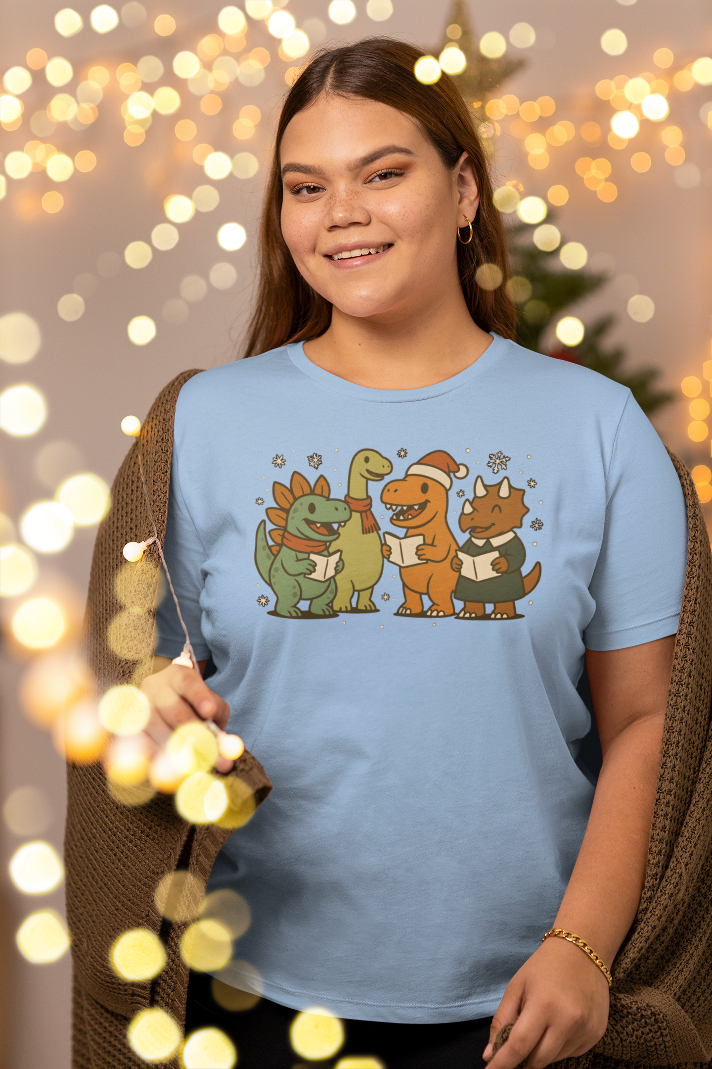 Dinosaur Carolers T-Shirt – Cute Dino Christmas Singing Tee in baby blue, shown on woman under warm festive lights