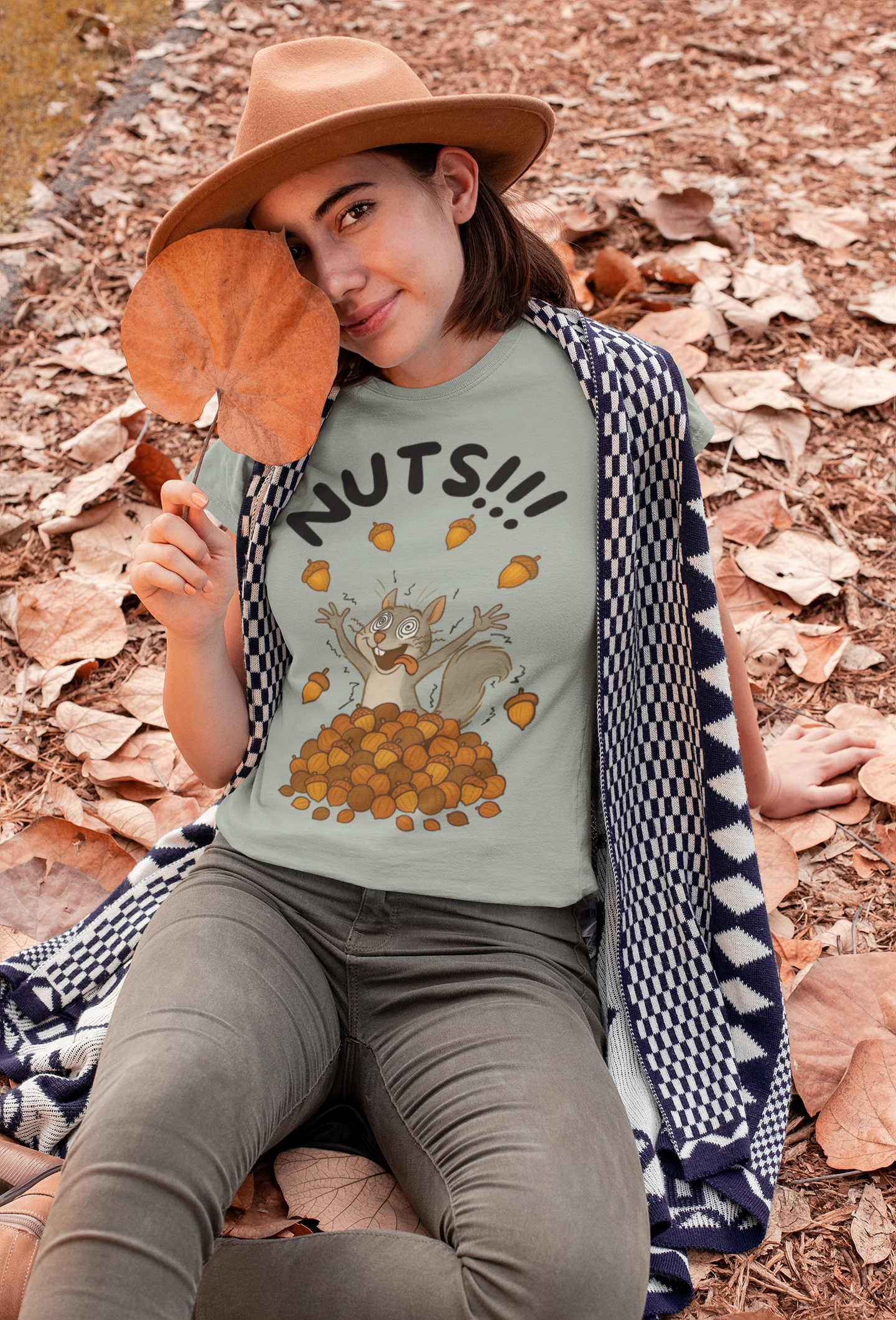 Crazy Squirrel Shirt – Funny Squirrel Nuts T-Shirt for Quirky Style shown on a woman lounging in autumn leaves while holding a giant dried leaf and smiling under a tan hat