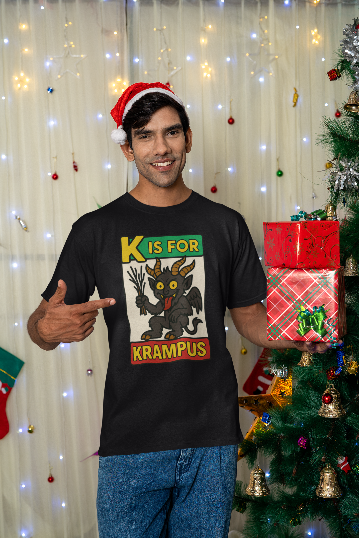 K is for Krampus Alphabet Holiday Graphic T-Shirt in Black worn by man celebrating Christmas next to tree and ornaments