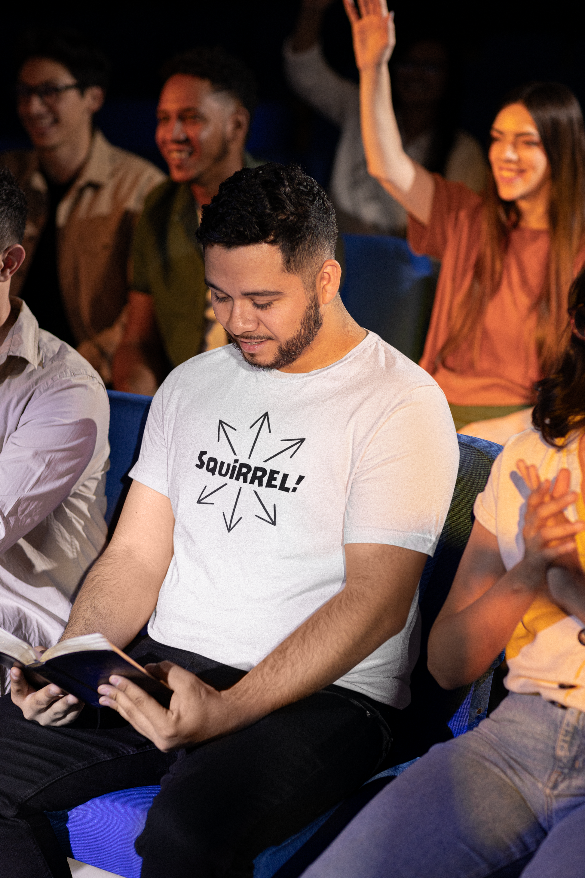 Squirrel Distracted Mind T-Shirt – Funny Attention Graphic Tee worn by a man reading a book in an audience, featuring a humorous squirrel shirt design about distraction and a wandering mind.