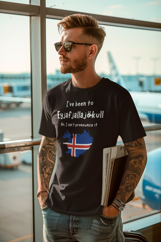 Lifestyle image of a man wearing the Eyjafjallajökull T-Shirt – Funny Iceland Volcano Travel Merch in black at an airport terminal, featuring the Icelandic flag over a silhouette of the country with humorous text about pronunciation.