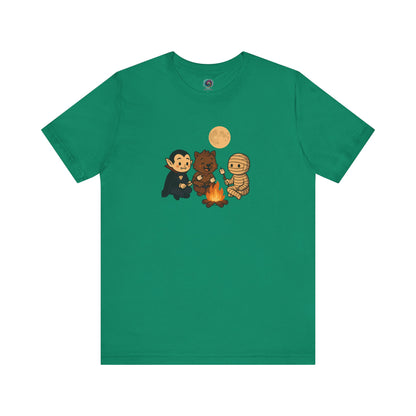 Halloween Monsters Campfire T-Shirt in Kelly showing a playful trio of costumed monsters roasting marshmallows in a cozy Halloween scene.