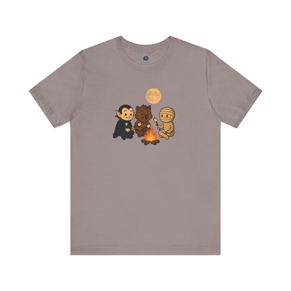Halloween Monsters Campfire T-Shirt in Pebble Brown from WhimSpin showing a trio of adorable monsters—vampire, werewolf, and mummy—roasting marshmallows under a full moon.