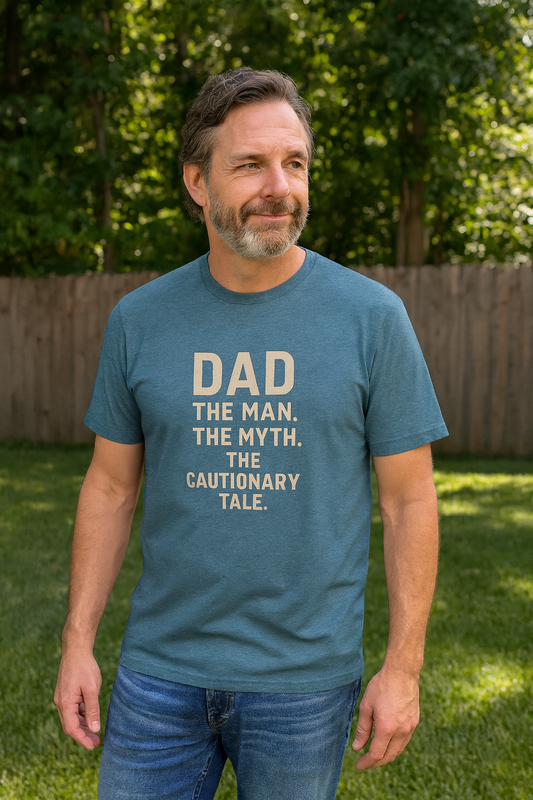 Dad T-Shirt – The Man. The Myth. The Cautionary Tale. worn by a bearded man standing in a grassy backyard, casual Father's Day outfit. 