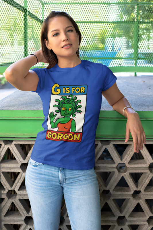Woman outdoors wearing the G is for Gorgon T-Shirt in blue, a halloween gorgon shirt with playful cartoon gorgon head artwork.