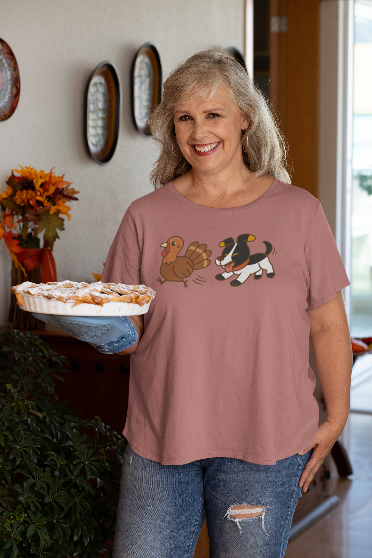 Dog Chasing Turkey T-Shirt – Funny Thanksgiving Dog Tee in pink, worn by older woman holding a pie in cozy home