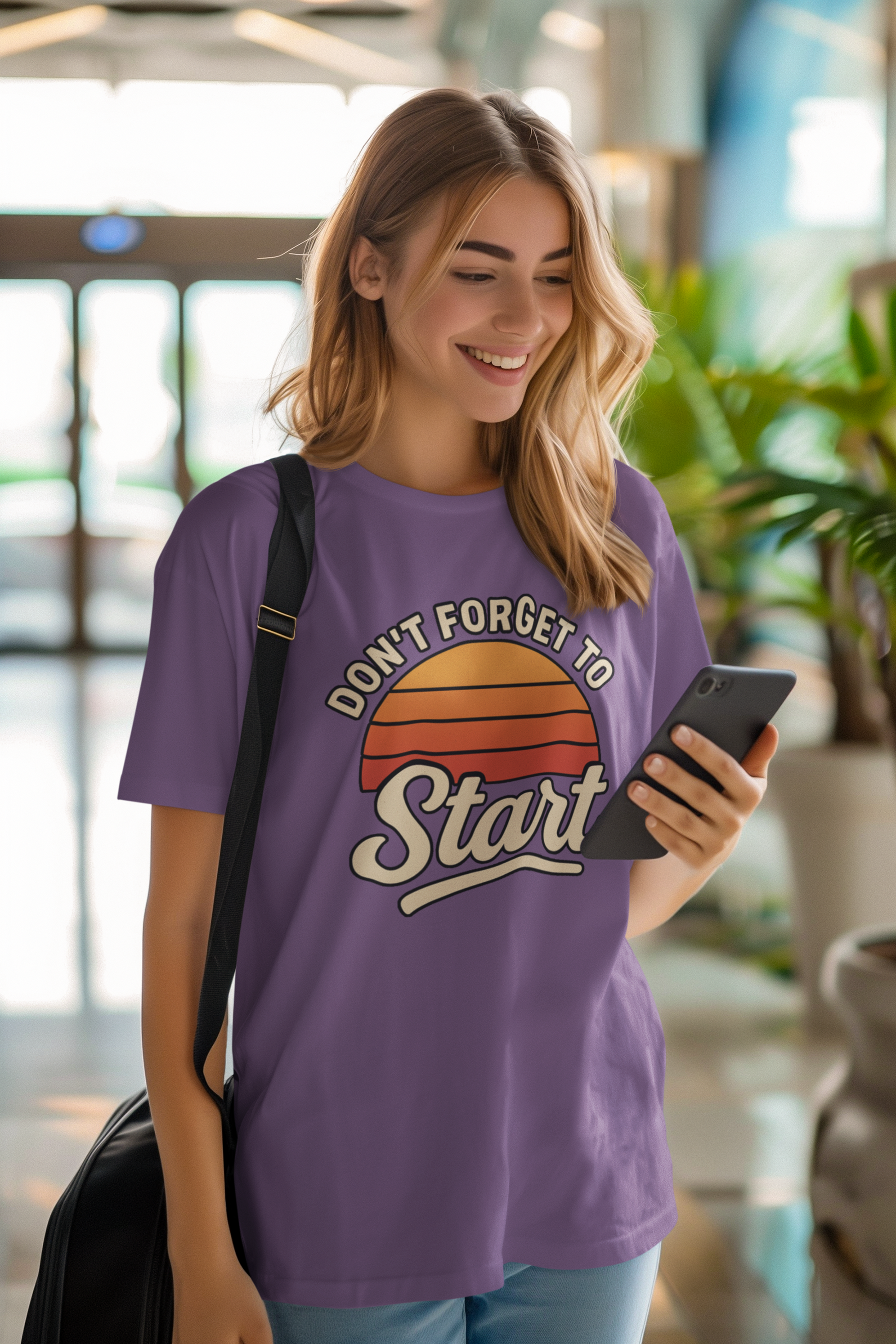 Don’t Forget to Start T-Shirt – Motivational Graphic Tee for Dreamers worn by happy woman texting in bright interior space with modern decor