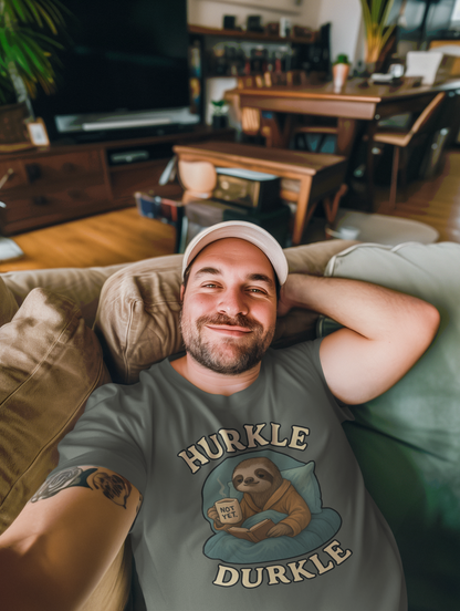 Hurkle Durkle Sloth T-Shirt – Cozy Sloth Shirt for Lazy Days shown in Heather Military Green worn by a relaxed man reclining indoors, showcasing cozy sloth holding a “Not Yet” mug