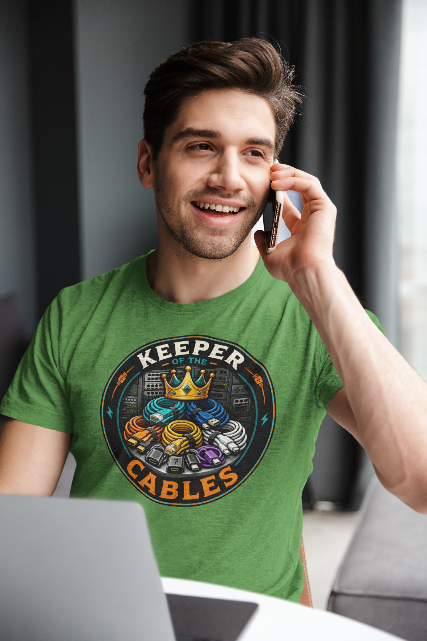 Man wearing a green t-shirt with 'Keeper Cables' logo, talking on a phone indoors. tech humor tee