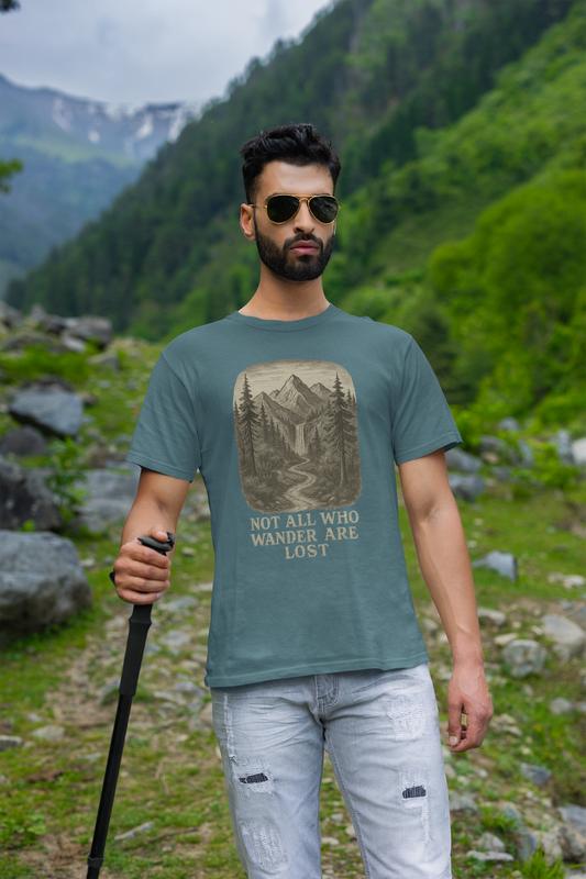 Man in sunglasses hiking a rocky mountain trail in heather deep teal “Not All Who Wander Are Lost T-Shirt – Tolkien Travel Tee for Nature Lovers” with scenic waterfall and forest graphic