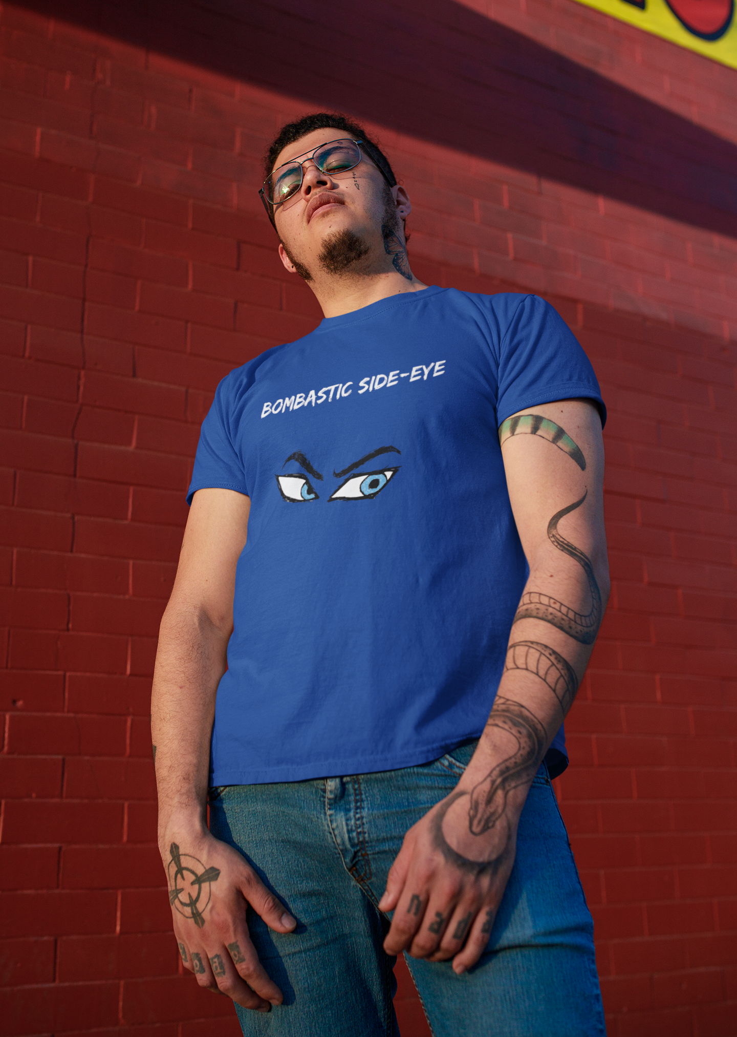 A man wearing the Bombastic Side-Eye T-Shirt – Comic Book Style Meme Graphic Tee in True Royal, standing against a brick wall with the vivid eye illustration centered.