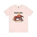 T-Rex Push-Up T-Shirt – Funny Dinosaur Workout Graphic Tee in soft pink with a cute yet fierce t rex hates push ups joke for quirky gym-goers.