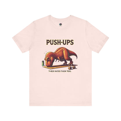T-Rex Push-Up T-Shirt – Funny Dinosaur Workout Graphic Tee in soft pink with a cute yet fierce t rex hates push ups joke for quirky gym-goers.