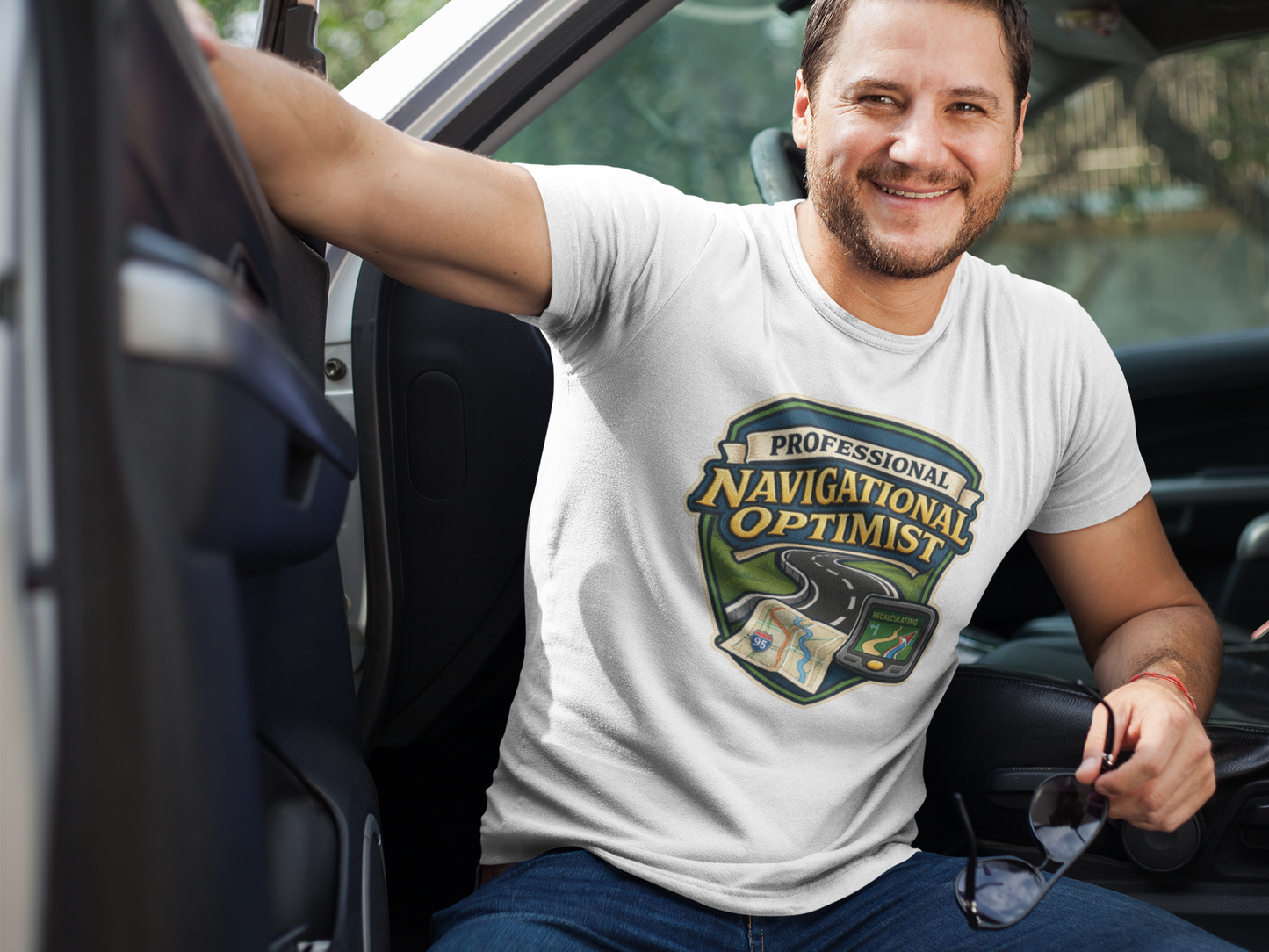 Man wearing a 'Professional Navigational Optimist' t-shirt in white sitting in a car.