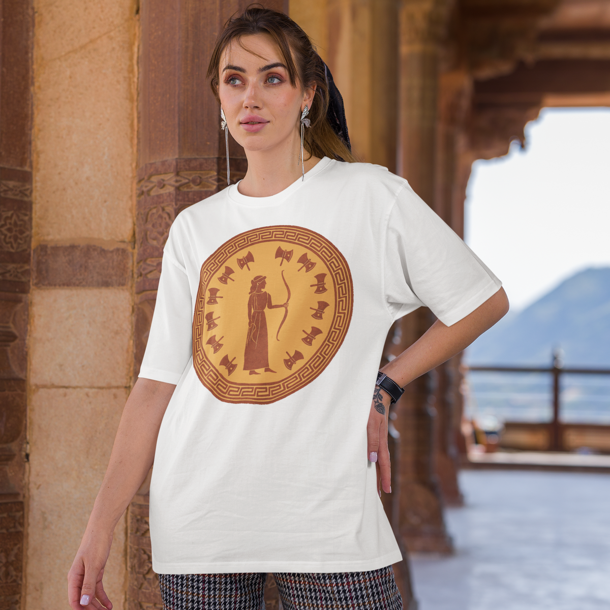 Woman at a classical structure wearing a white Penelope Queen of Ithaca t-shirt with ancient Greek pattern, a literary tribute tee.