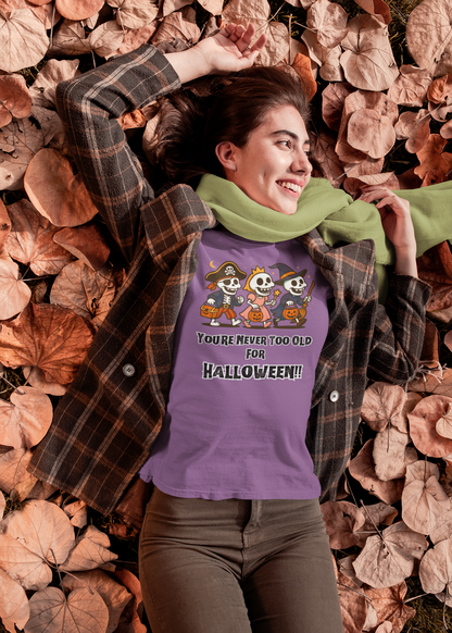 Woman in a plaid jacket and scarf relaxing in dried leaves, wearing the Never Too Old for Halloween T-Shirt – Funny Adult Halloween Shirt in heather team purple; a fun adult Halloween design celebrating spooky season.